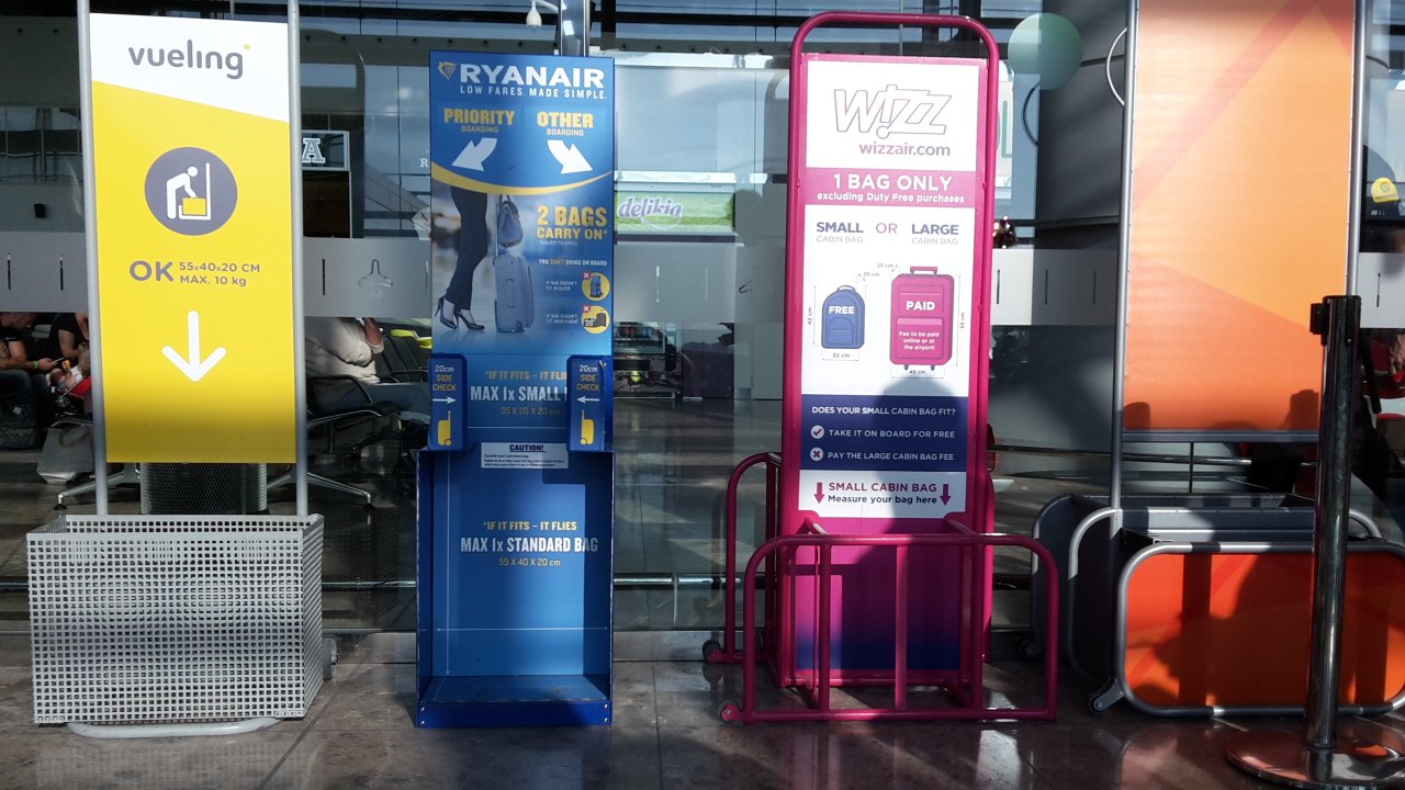 Medidores de equipaje de mano de varias aerolíneas en un aeropuerto, con marcos de distinto tamaño.